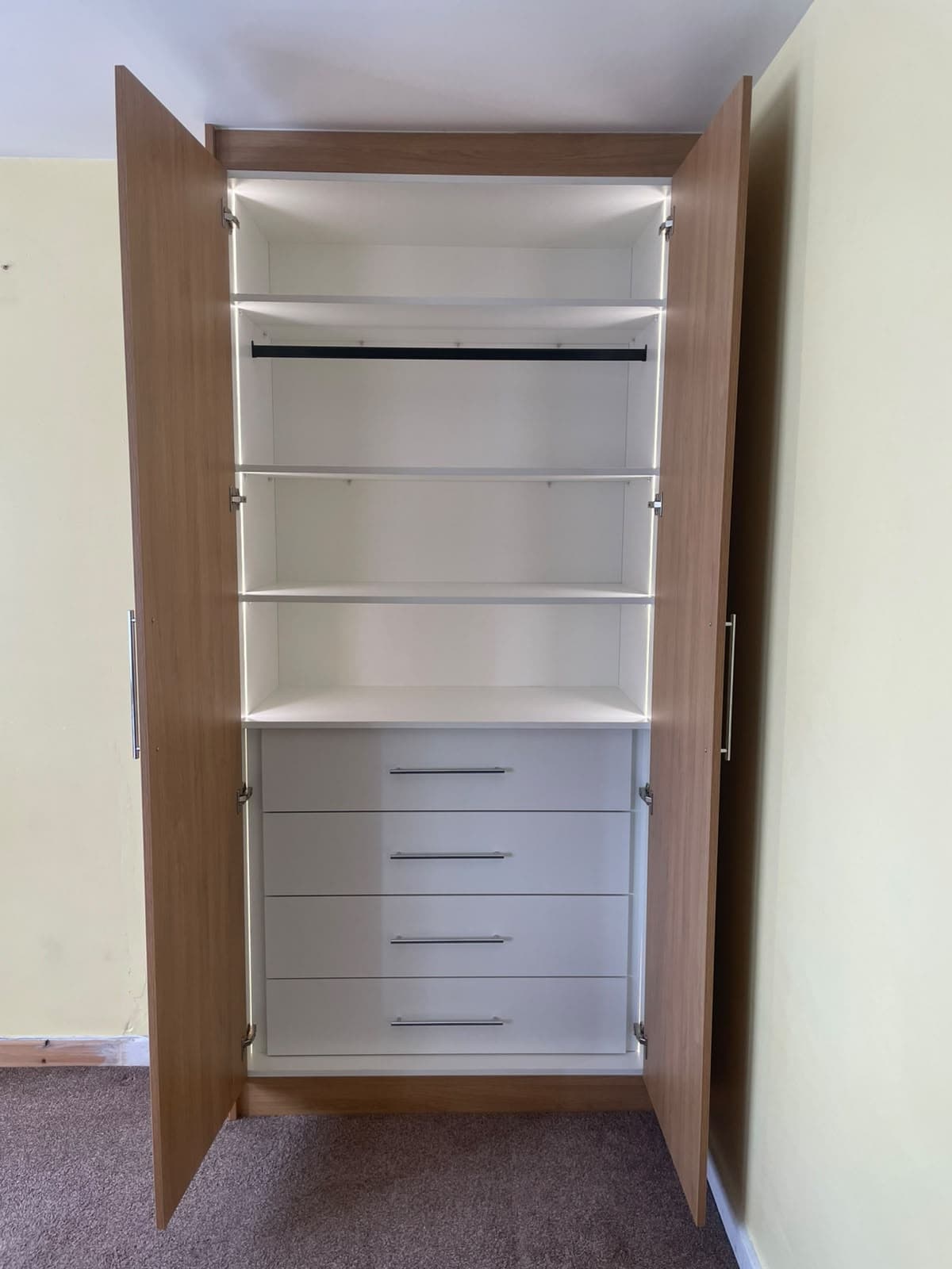 Wardrobe interior showing hanging rail, shelves and six-drawer chest with LED lighting
