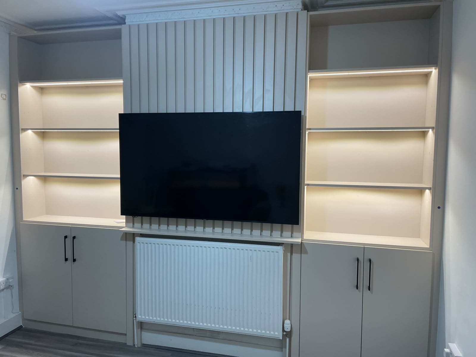 Full-width bespoke media wall with fluted centre panel, large TV recess, LED-lit open shelving and lower cabinets with matte black handles