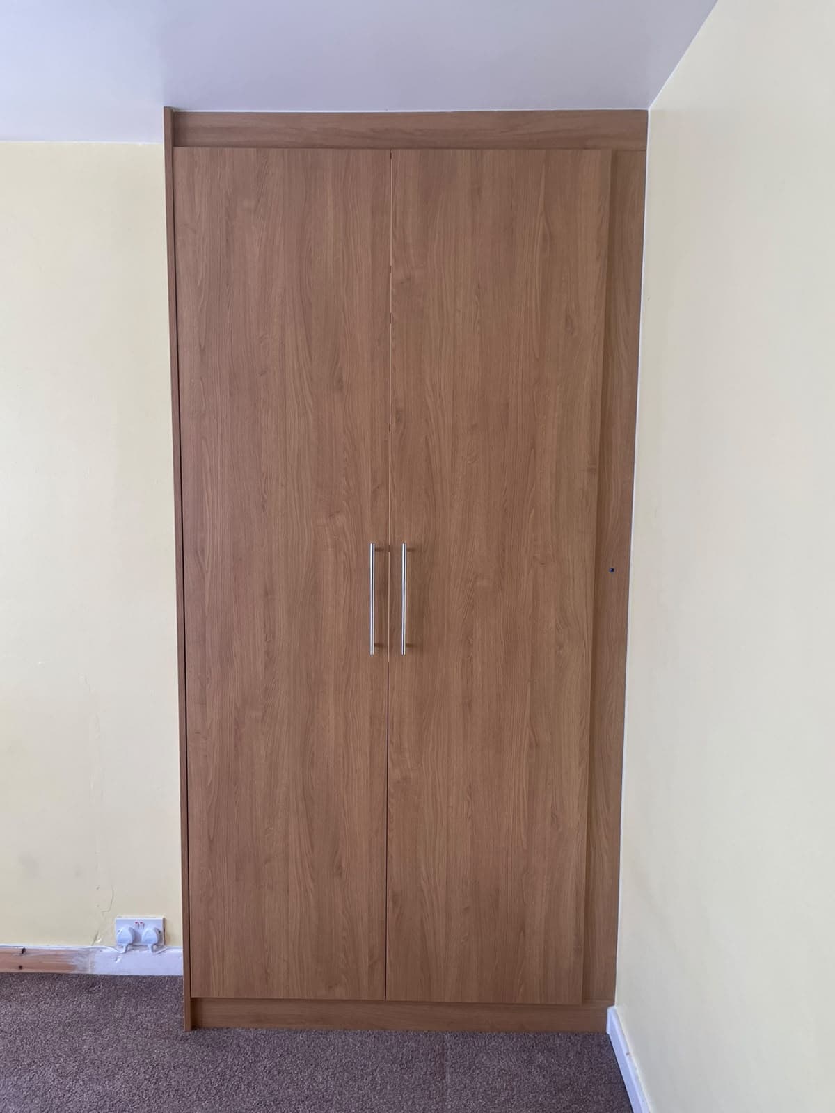 Fitted wardrobe in warm oak finish with brushed steel bar handles